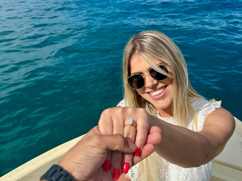 Client showing custom engagement ring on boat over turquoise water, Sakaris Jewelers Naples Florida
