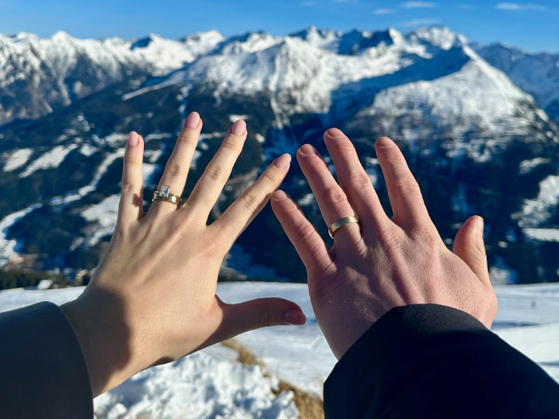 Couple showing custom engagement ring and wedding band by Sakaris Jewelers with snowy Alps behind