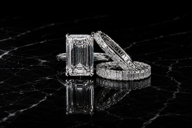 Emerald cut diamond engagement ring with baguette eternity wedding bands on black marble, Sakaris Jewelers Naples Florida custom design studio